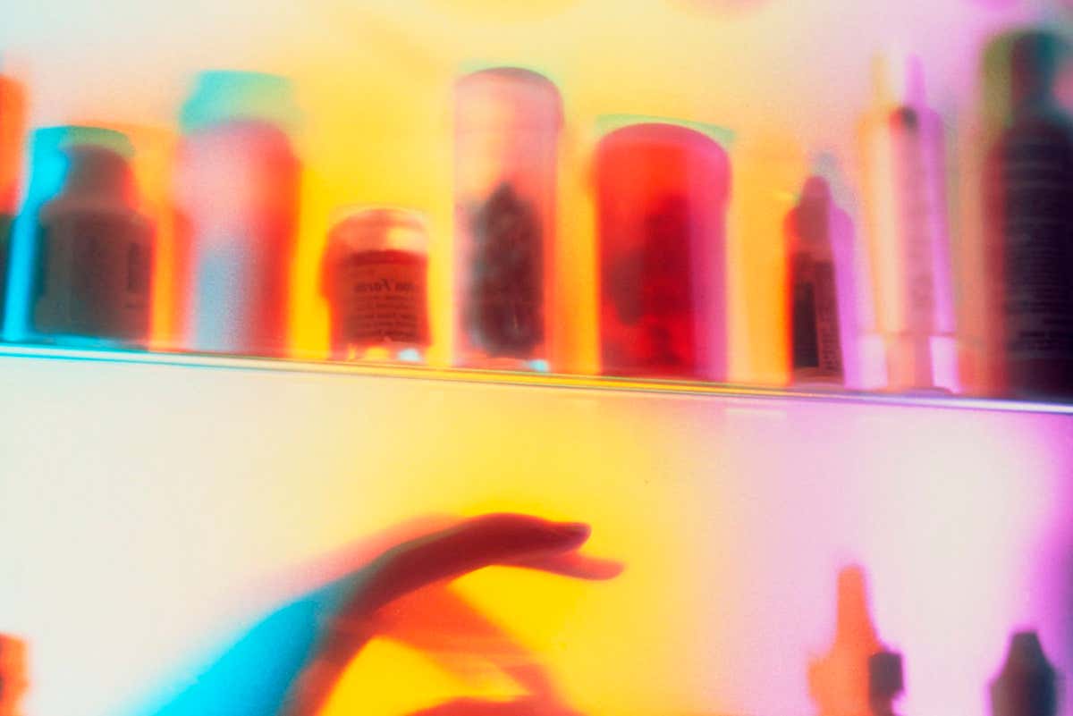 Drug dependency. A hand reaches into a medicine cabinet in this abstract view of drug addiction. Psychedelic colours and a blurring of the image gives a hallucinogenic effect.